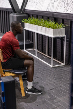 Man is resting on wooden bench in modern gym lounge area, with white planter and mural
