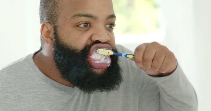 African American man starting with retractor, pressing toothbrush with foam, brushing teeth at sink