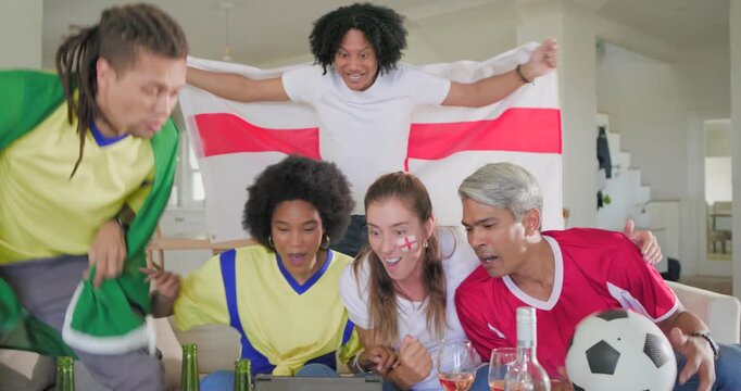 Diverse friends huddling on couch watching tablet celebrating goal swapping flags holding ball