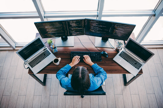 Professional coder at multi screen workstation in a modern loft office coding on multiple monitors