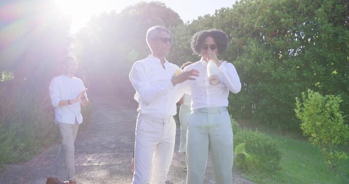 Diverse group walking path, two men stepping and hugging, celebrating, holding bottle and pin