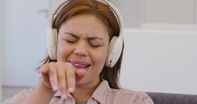 African American woman in pink top headset hearing music mouthing moving fingers-to-arms on couch