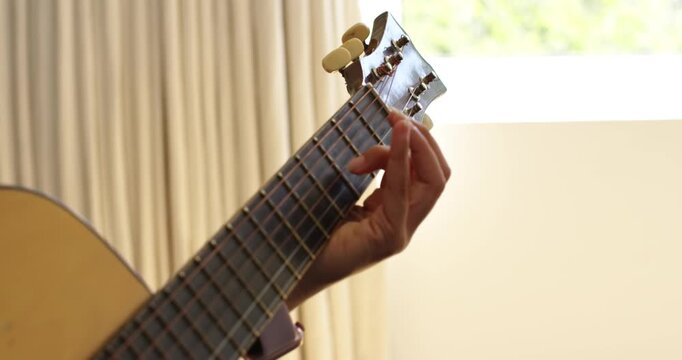 African American woman practicing acoustic guitar, moving left hand along fretboard to learn song