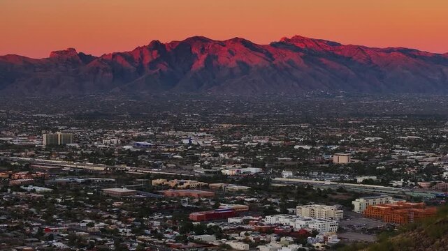 Aerial view of buildings and mountains in the distance, with a warm sunset sky over the vast cityscape, Tucson, Arizona, United States.
