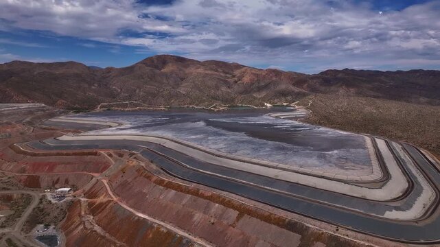 Aerial view of terraced tailing ponds with contrasting red earth and grey water, nestled against a backdrop of rugged mountains, Tucson, Arizona, United States.
