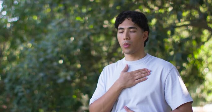 Man practicing slow focused breathing in park, placing hand on chest and abdomen for health