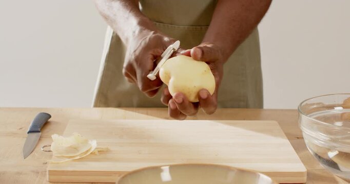 African American man in tan apron picking Y-shaped peeler peeling potato while rotating for cooking