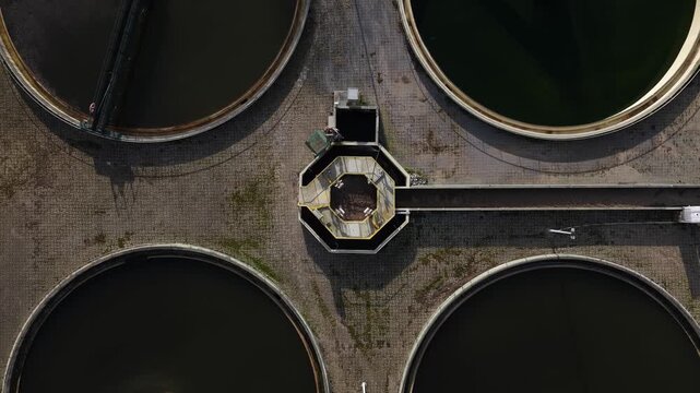Aerial view of circular sewage treatment plant with dark water and mechanical arms, contrasting textures, Lisbon, Portugal.