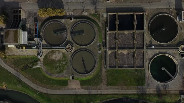 Aerial view of a water treatment plant showcasing circular and rectangular tanks, reflecting earthy tones against a backdrop of concrete and greenery, Lisbon, Portugal.