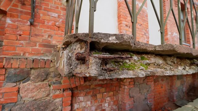 Close-up of a deteriorating balcony slab on an old brick building, showing crumbling concrete, exposed rebar, rusted steel, and a failed patch repair&mdash;urban safety concept.