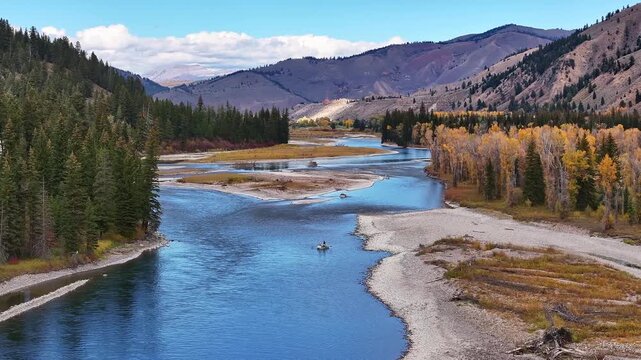 River bend with sandy shoreline and autumn forest in Wyoming valley, fisherman on kayak floats slowly, aerial telephoto tracking right
