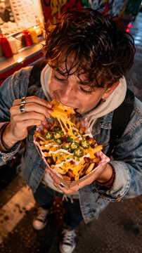 Loaded cheesy fries street food editorial photography of college student taking first bite in food alley