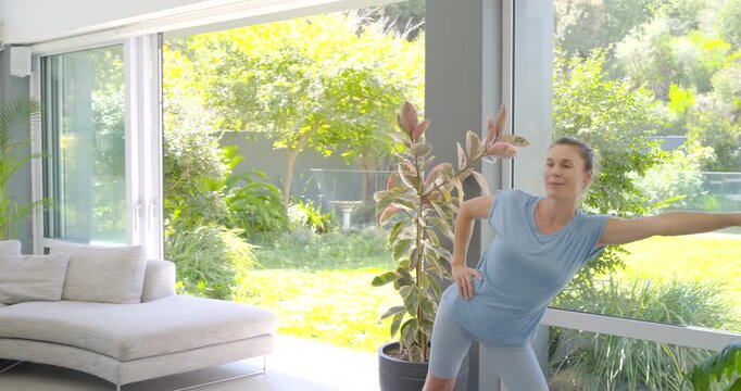 Mid-adult female trainer starting arm extension at window, guiding men into triangle stretch on mat
