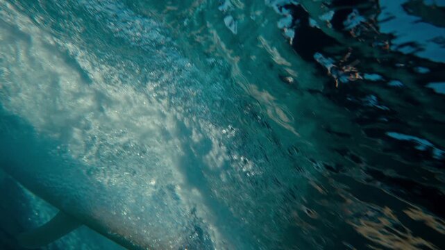 Inside ocean wave barrel with sunlight shining through translucent water shimmering surfer riding longboard, abstract background