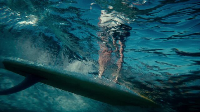 Underwater perspective of surfer riding wave above on single fin longboard surfboard, slow motion tracking follow