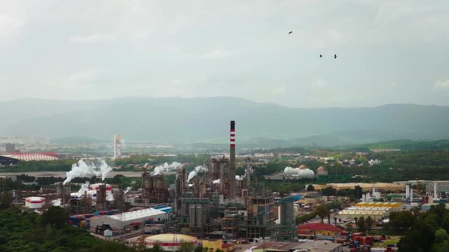 Aerial view of an industrial complex with chimney stacks releasing white smoke, against a backdrop of distant mountains, San Roque, Andalusia, Spain.