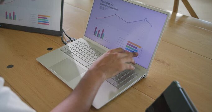 Man sitting left at wooden table, after chart update tapping and typing on laptop, copy space