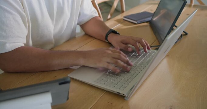 Hands landing on keyboard, mid adult African American man typing on silver laptop completing work