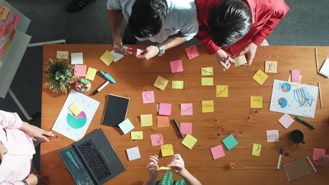 Top down aerial view of business team brainstorming idea and writing plan at colorful sticky notes. Professional project manager planning strategy while stick paper at meeting table. Convocation.