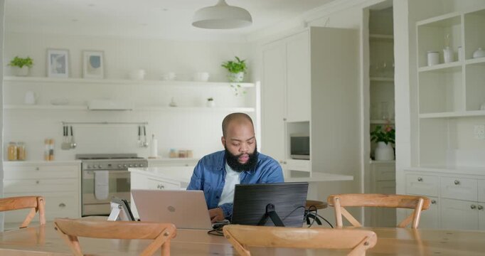 African American man blue-shirted sitting in kitchen responding to email on laptop and monitor
