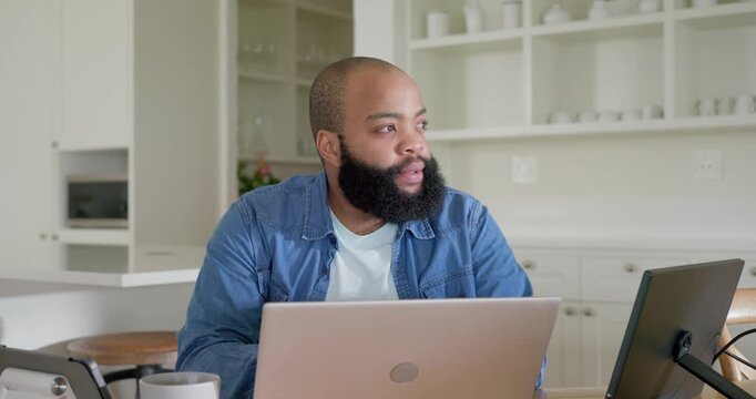 African American man in kitchen hearing ping leaning reading laptop yawning typing with screen