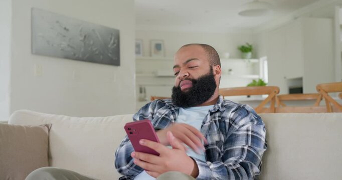 African American man sitting on sofa, checking red-cased smartphone after seeing surprising message
