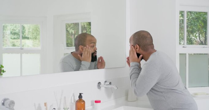 Man standing at bathroom sink grooming beard in mirror, wearing light grey shirt, copy space