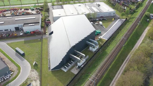Aerial view of datacenter covered in solar panels, with a railroad track running alongside it, creating a contrast between industry and nature, Oostkamp, Flanders, Belgium.
