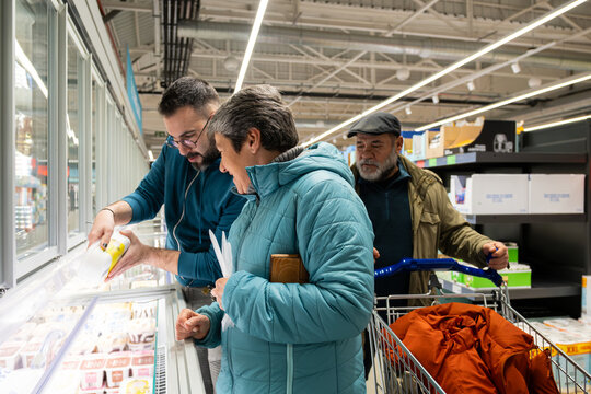 Family comparing frozen food products from a freezer display in a grocery store