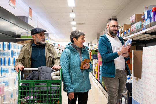 Three generations of adults shopping together, choosing products in a brightly lit grocery store