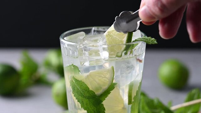 Placing lime slice on mojito cocktail glass with fresh mint
