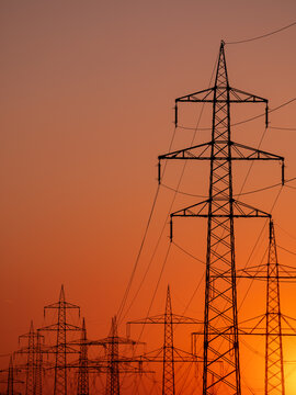 Silhouette of several high-voltage power lines and electricity pylons against a glowing orange and red sunset sky in Germany.