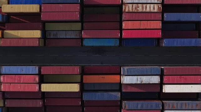 Alicante, Spain - 11 April 2026: Aerial view of colorful shipping containers stacked high, separated by a dark road, creating a geometric pattern.