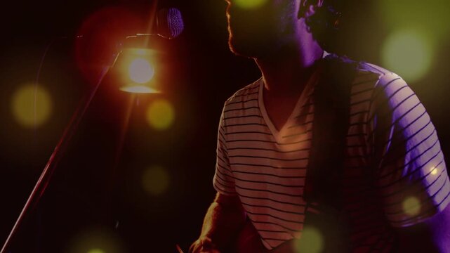 Camera pulling back, musician playing red guitar and singing into mic, performing under amber lamp