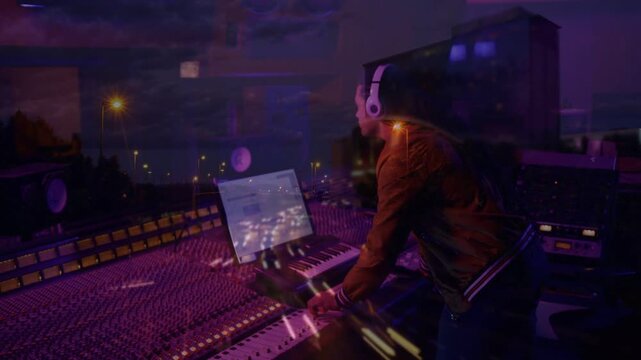 Music producer cueing laptop playback and balancing mix at console, city lights overlay syncing