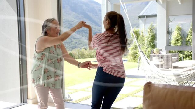 Sunlit room showing older woman lifting hand to invite twirl, guiding teen spinning into family hug