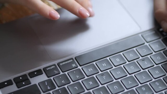 Close-up of hand on laptop touchpad. Fingers gently move across silver trackpad. Keyboard visible below, showing Cyrillic characters. Natural light highlights smooth surface