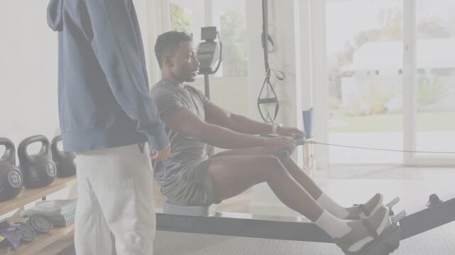 Seated rower starting strokes on slide machine while coach supervising training near kettlebells