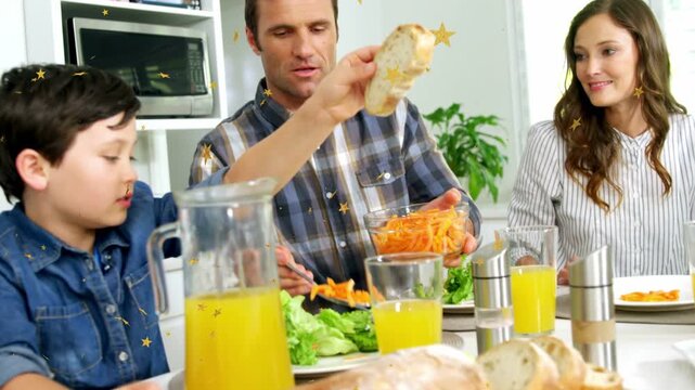 Boy reaching for bread causing man scooping carrots, family sharing food at kitchen table
