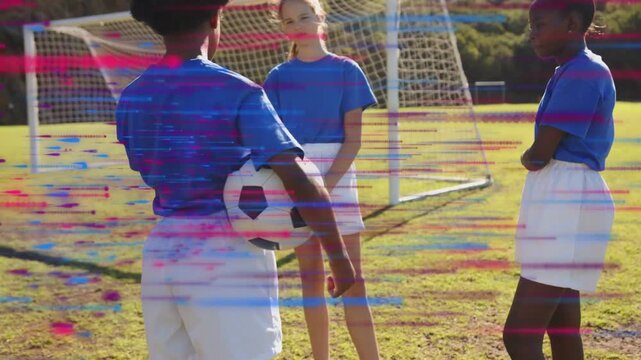 Three girls standing on soccer field by goal, one holding ball, planning and sparking motion arrows