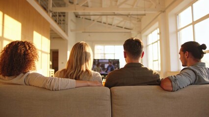 Obraz premium Group of four young adults sitting on large gray sofa watching televis.