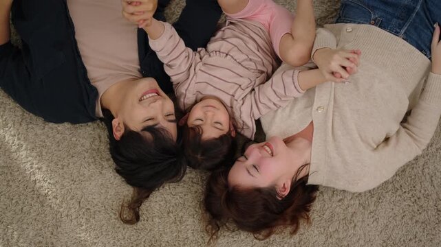 Joyful Asian family with little daughter lying together on carpet at home