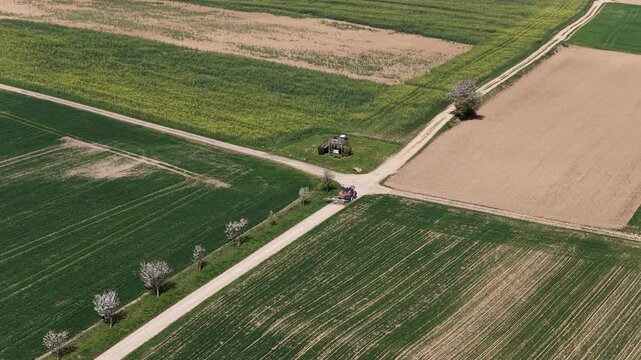 Aerial view of vibrant agricultural fields intersected by pathways, revealing a tractor and small building nestled amid the colorful landscape, Wintzenheim-Kochersberg, France.