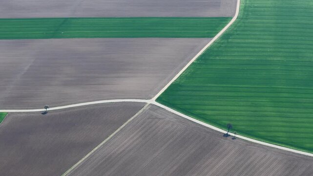 Aerial view of a patchwork of green and brown fields bisected by pale pathways, creating a geometric tapestry of agricultural lands, France.