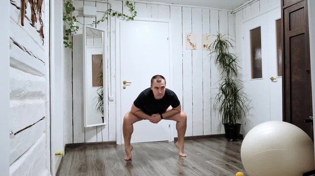 Caucasian man doing sumo squats lifting heels. Person does sport exercise at home. Hard workout. Morning warmup. Strengthening the legs muscles. Strong body. High quality 4k footage.