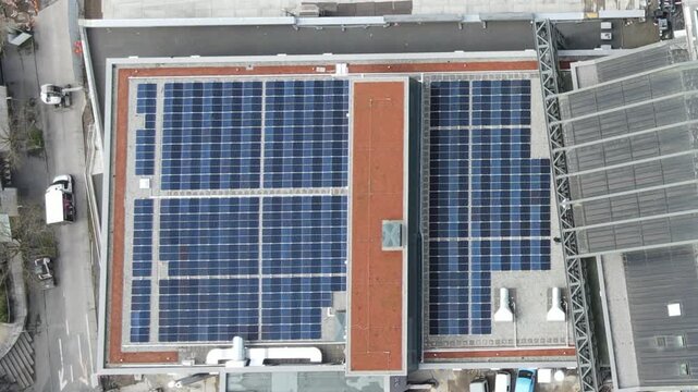 Static top-down aerial drone view of rooftop solar panels on modern buildings, forming a geometric pattern representing renewable energy and sustainable urban infrastructure.