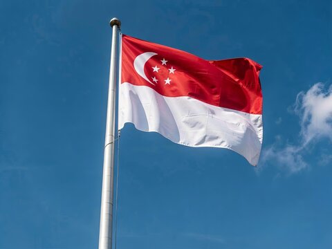 Singapore national flag flying on silver pole against clear blue sky with scattered clouds.