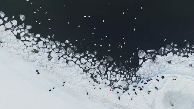 Aerial view of the Baltic sea with ice floes creating a stark contrast against the dark water, with people on the snowy shore, Sopot, pomorskie, Poland.