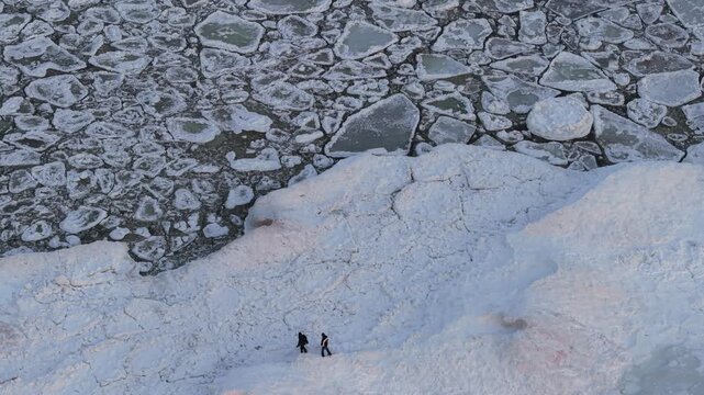 Aerial view of the frozen Baltic sea, where icy waters meet the snow-covered shore, with two figures standing on the ice, Mikoszewo, pomorskie, Poland.