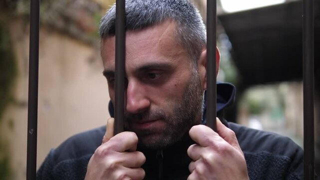 Young man holding gate looking very sad and alone. Emotional outdoor scene expressing loneliness, confusion and inability to find a solution.